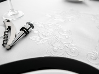 Metal wine opener and bottle stopper on white ornamented tablecloth