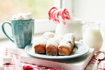 Christmas muffins, milk, cocoa, marshmallows, candy lollipops on a white plate by the window