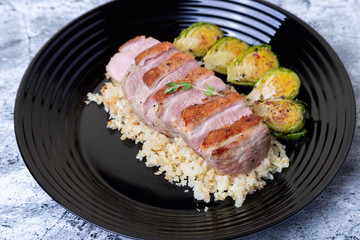Grilled duck with fried Brussels sprouts, rice from cauliflower on a black plate. Close-up, selective focus.