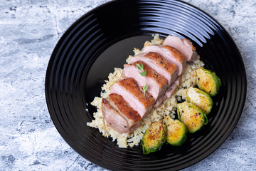 Grilled duck with fried Brussels sprouts, rice from cauliflower on a black plate. Close-up, selective focus.