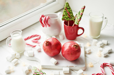 Christmas sweets pomegranate, milk, marshmallows, candies on a white background by the window