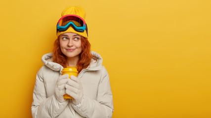 Pensive dreamy foxy woman has coffee break after skiing, warms with hot beverage during winter...