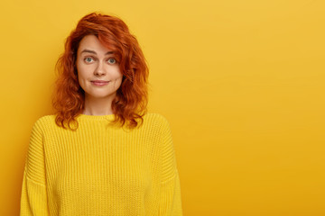 Portrait of young ginger woman has natural beauty, dressed in yellow knitted jumper, dimples at...