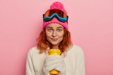Girl snowboarder wears warm winter outfit, white mittens, holds takeaway coffee, has sporty...