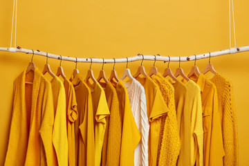 Set of bright yellow clothes and one white sweater on hangers. Collection of womens attires to wear. Variety of outfits for warm and hot weather. Wadrobe closet. Fashion, shopping and consumerism