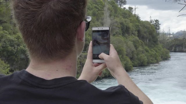 An over the shoulder shot of someone taking photos on a phone of the Huka  Falls in Taupo, NZ.