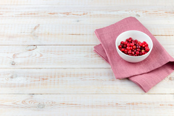 Red cranberries in a white bowl on old white rustic wooden background with copy space