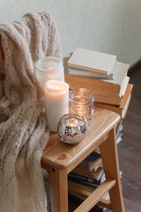 Warm knitted plaid blanket, candles, book and wooden chair - cozy home relax interior, autumn winter seasonal leisure time, hygge interior, copy space, monochrome