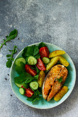 Vegetarian lunch or dinner, healthy eating concept. Grilled salmon, rustic baked potatoes and salad with fresh vegetables on a stone countertop. Top view flat lay background with copy space.