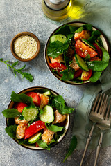 Tasty and healthy Salmon Grilled Salad with cucumber, tomatoes, fresh arugula and sesame seeds on a gray stone table. Top view flat lay background.