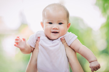 Smiley face of newborn baby feeling happy and smiles with her mother in the garden. Portrait of Asian family.