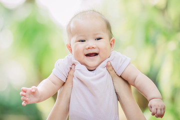 Smiley face of newborn baby feeling happy and smiles with her mother in the garden. Portrait of Asian family.