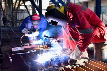 Two welder is assembling the workpiece by process shielded metal arc welding (SMAW). Welder in red...