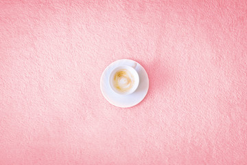 Cup of coffee on a pink background. A cappuccino in a white cup is centered on a pink bedspread or rug.