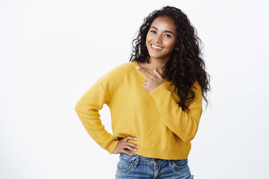 Carefree modern young african-american girl with curly hair in yellow sweater, tilt head joyfully smiling, look camera as discuss cool new promo, pointing left blank space over white background