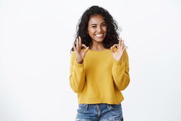 Cheerful pleased dark-skinned girl student in yellow sweater smiling with approval and delight, show okay good gesture, rate excellent promo, recommend great app, looking satisfied, white background