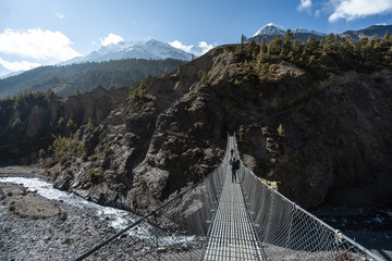 Trekker enjoying good weather in time of trekking through Annapurna Circuit while going by a suspension bridge.