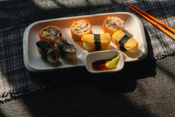 Sushi on a white plate chopsticks on the wooden table by the window in kitchen with morning sunlight, Black background and tableware, Selective focus.