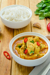 Spicy chicken breast in yellow curry sauce with garlic and chili  pepper with boiled rice in a bowl on a dark wooden background.