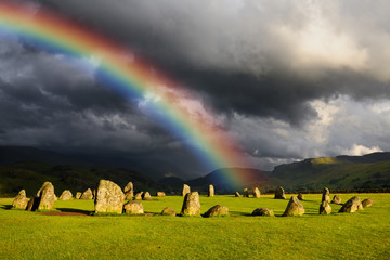 Rainbow over Castlerigg Stone Circle on summer solstice eve with sun and dark clouds over Cumbrian...