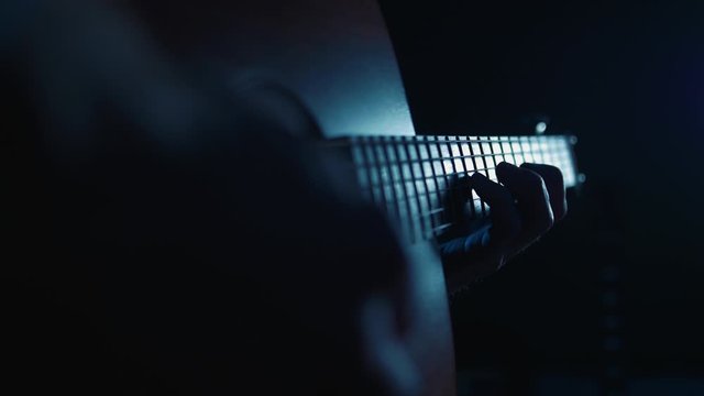 Guitarist playing acoustic guitar, lit by eerie blue lights
