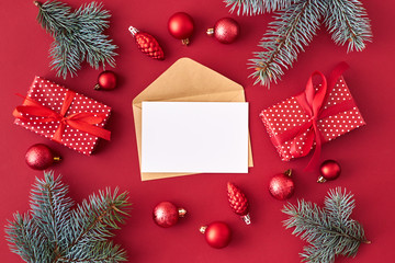 Fototapeta na wymiar Mockup white greeting card and envelope with red christmas balls, spruce branches and gift box on a red background