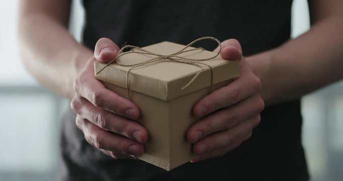 Slow motion young man shows brown craft paper gift box