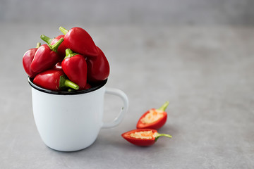 Red chili peppers in a white metal mug on a gray background.
