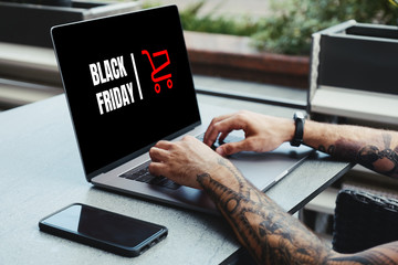 Black Friday banner in a laptop computer while man shopping online in coffee shop.