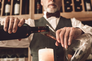Sommelier Concept. Senior man standing pouring wine into decanter above candle close-up - obrazy, fototapety, plakaty