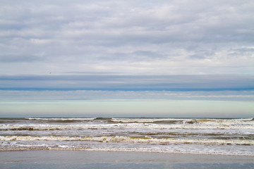 Horizontal lines of beach, sea, waves, clouds and blue sky