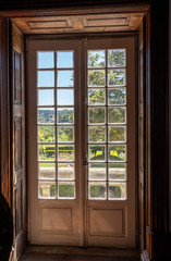 Wooden carved and glazed doors leading from old house into garden with sunlight
