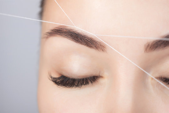 The make-up artist plucks eyebrows with a thread close-up. Women's cosmetology in the beauty salon.