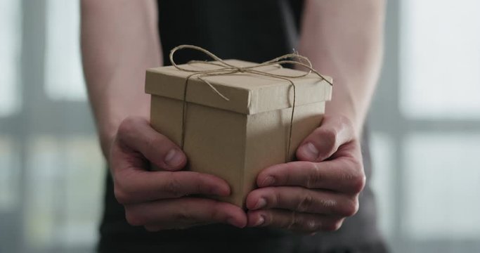 Slow motion young man shows brown craft paper gift box