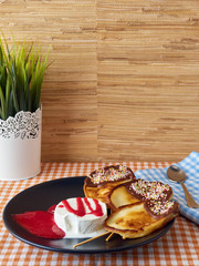 Three pancakes covered by chocolate and multicolored candies with ice-cream dressed by strawberry jam and putted on black dish.