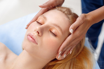 Fototapeta na wymiar Cosmetology Service. Young woman at beauty clinic lying closed eyes while doctor touching head preparation for procedure close-up