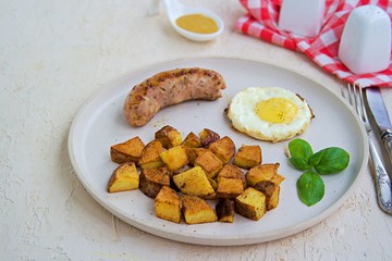 Large breakfast, home fries potatoes, pork sausage and fried egg on a white clay plate on a light concrete background. American food