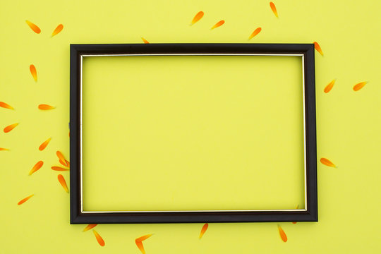 Photo frame on a yellow background with orange flower petals. Free space for an inscription.