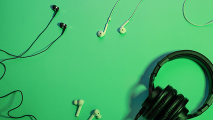 Headphones of different types flat lay on green color background, copy space. Black in ear headphones, wireless and foldable over ear headphones closeup with cable, music concept, top view.
