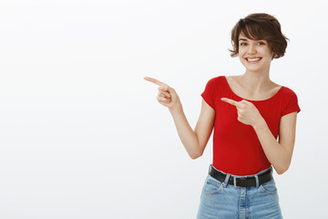 Girl inviting you come together check-out cool festival. Cheerful lucky cute alluring nice woman short stylish pixie haircut smiling broadly optimistic expression pointing index fingers left