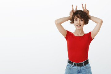 Funny carefree silly cute european girl short pixie haircut show bunny rabbit ears hold v signs...