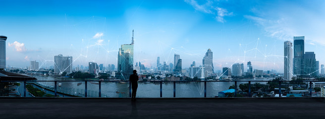 Businessman standing using smart phone in modern space watching city night view.Business Wireless network and Connection technology concept.