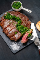 Ready to eat black Angus beef rib eye steak sliced with herbs, garlic and sauce on slate Board. Ready meal for dinner on the background of dark ebony.