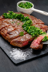Ready to eat black Angus beef rib eye steak sliced with herbs, garlic and sauce on slate Board. Ready meal for dinner on black wooden background