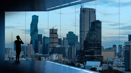 Businessman standing using smart phone in modern space watching city night view.Business with ambition and vision concept.