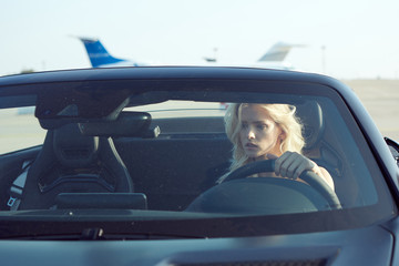 One glamorous blonde woman sit in cabriolet car, glamour girl inside cabrio auto on the runway. No retouch.