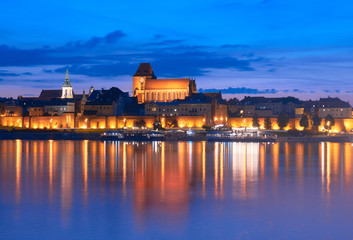 Torun old town in Poland, UNESCO world heritage site, with illumination, reflected in Vistula river at beautiful evening. - obrazy, fototapety, plakaty