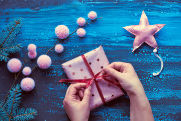 Female hands wrapping Xmas gift, winter decorations and fir twigs. Christmas flat lay in blue,...