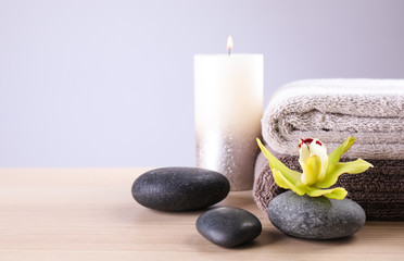 Fototapeta na wymiar Spa stones with exotic flower, burning candle and fresh towels on wooden table, space for text