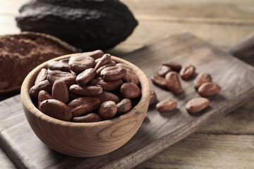 Bowl with cocoa beans on wooden table, space for text